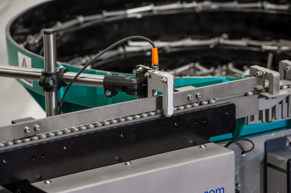 Conveyor belt feeding into a Sandfield Engineering vibratory bowl feeding system in a production line.